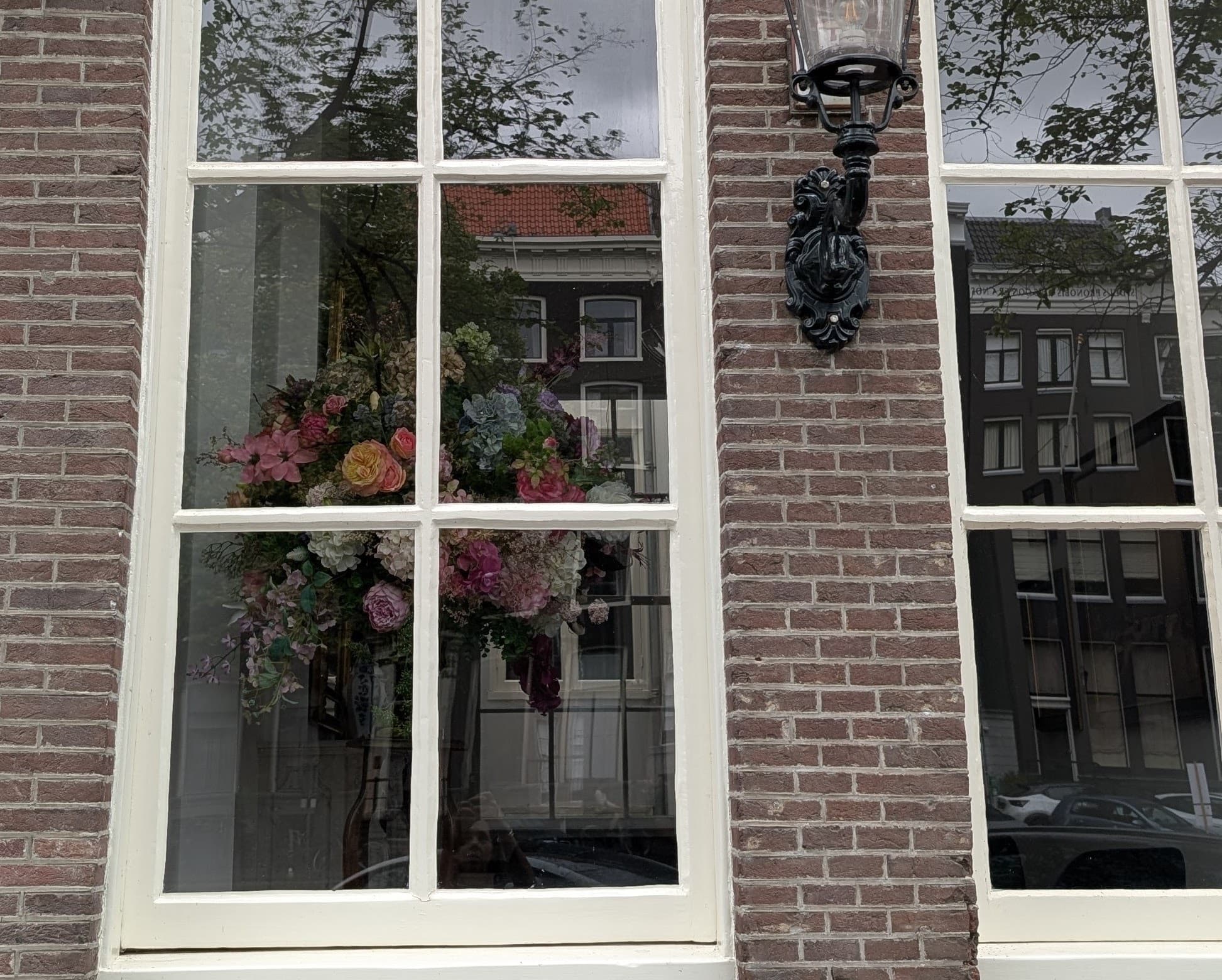 A lit canal house window in Amsterdam at dusk with a floral arrangement on the sill