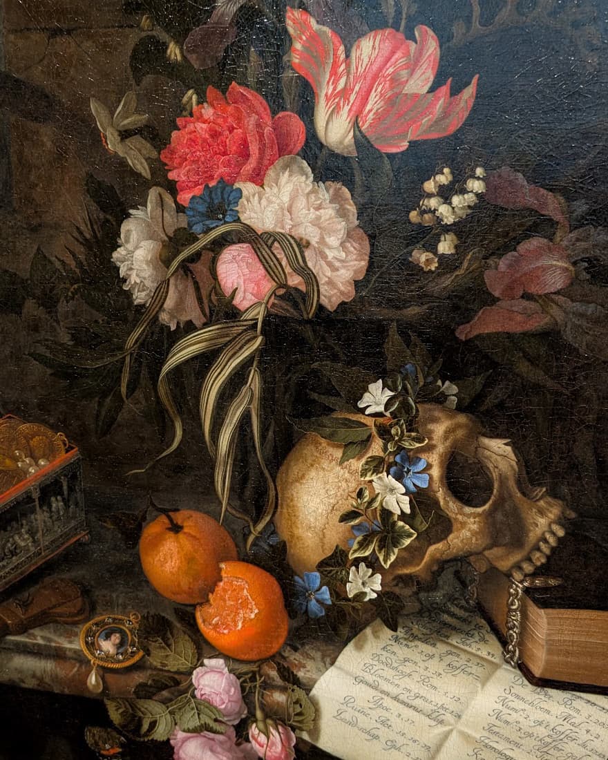 Detail of Maria van Oosterwijck's Vanitas Still Life, showing a bouquet of tulips, peonies and roses above a skull wreathed in flowers, with oranges and a handwritten note on a marble ledge